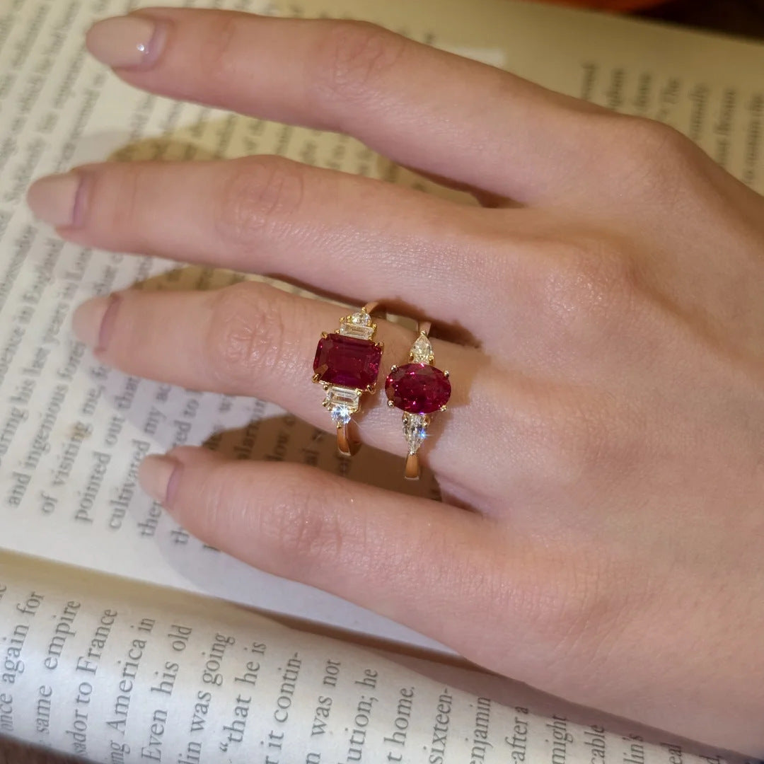 Two Red Gemstone Gold Rings worn side by side, emerald-cut and oval-cut settings, on a book