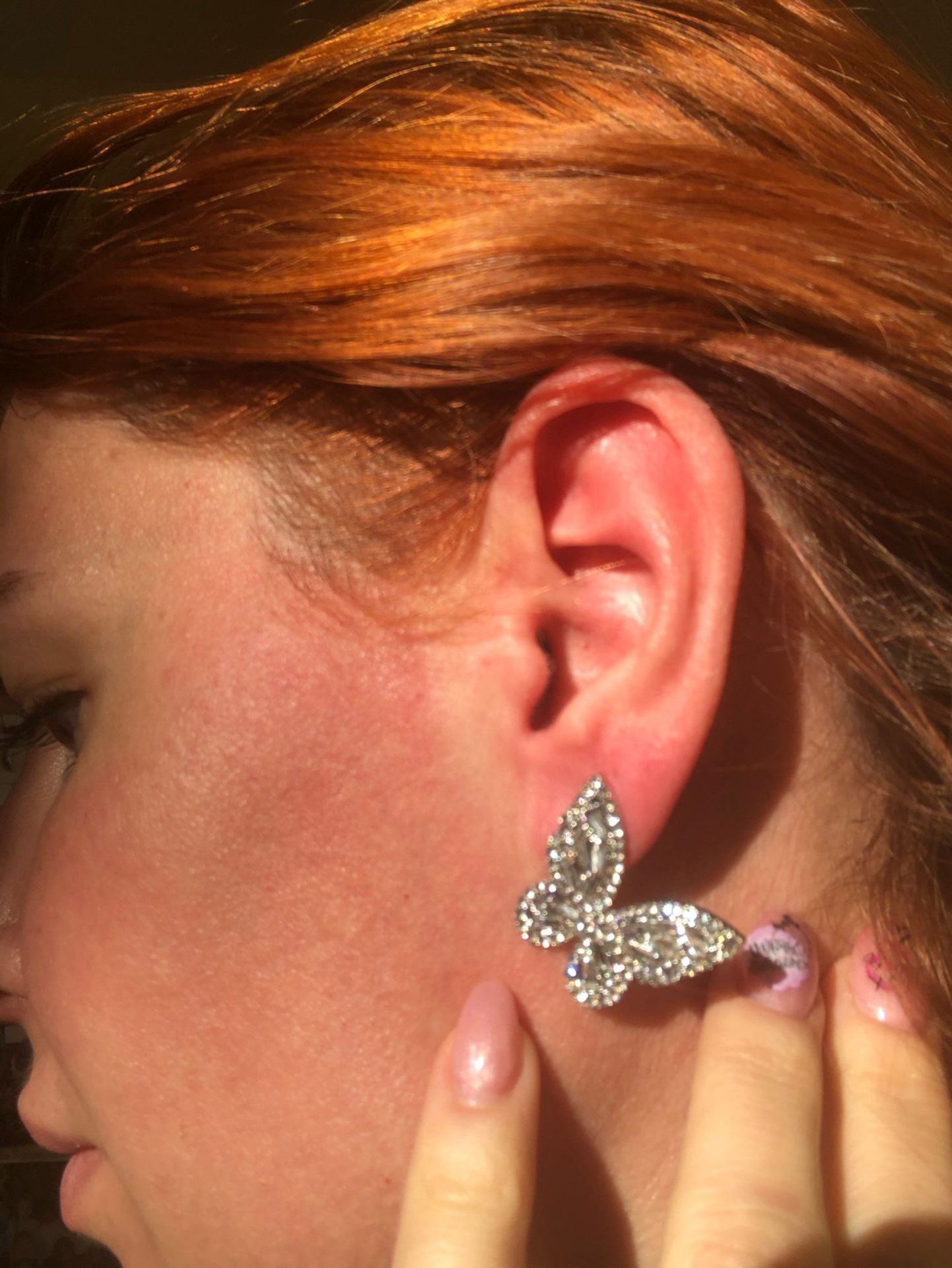 Model with red hair wearing silver crystal butterfly stud earring, close-up on ear