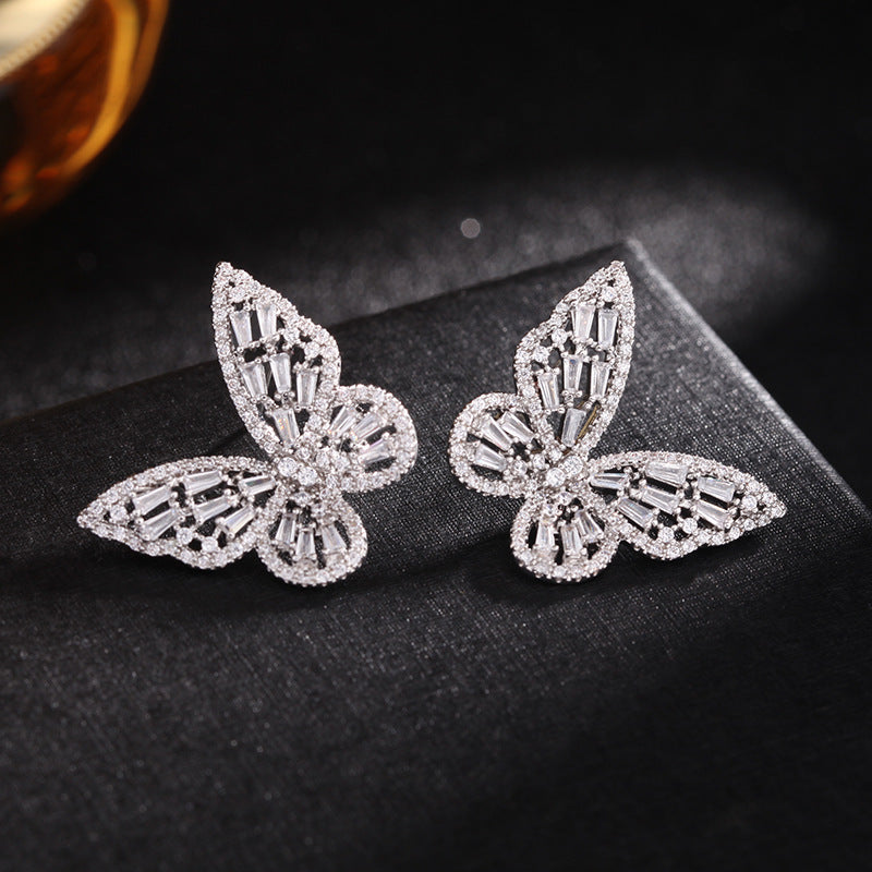 Silver crystal butterfly earring pair on dark textured fabric, pave-set baguette wings
