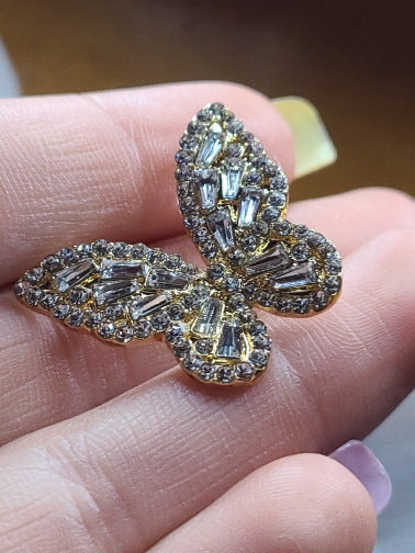 Crystal butterfly earring held in open palm, close-up detail of baguette-cut wings in gold setting