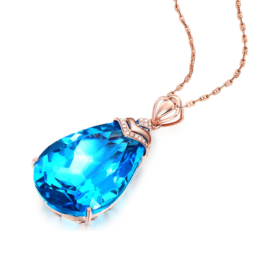 Blue Crystal Pendant Necklace on white background, prong-set blue topaz with diamond bail and coiled rose-gold chain