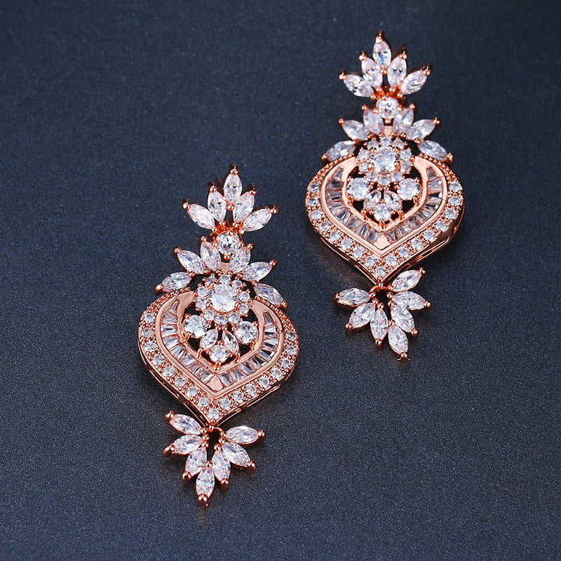 CZ Flower Drop Earrings in rose-gold tone, cubic zirconia heart-flower design laid flat on dark blue background