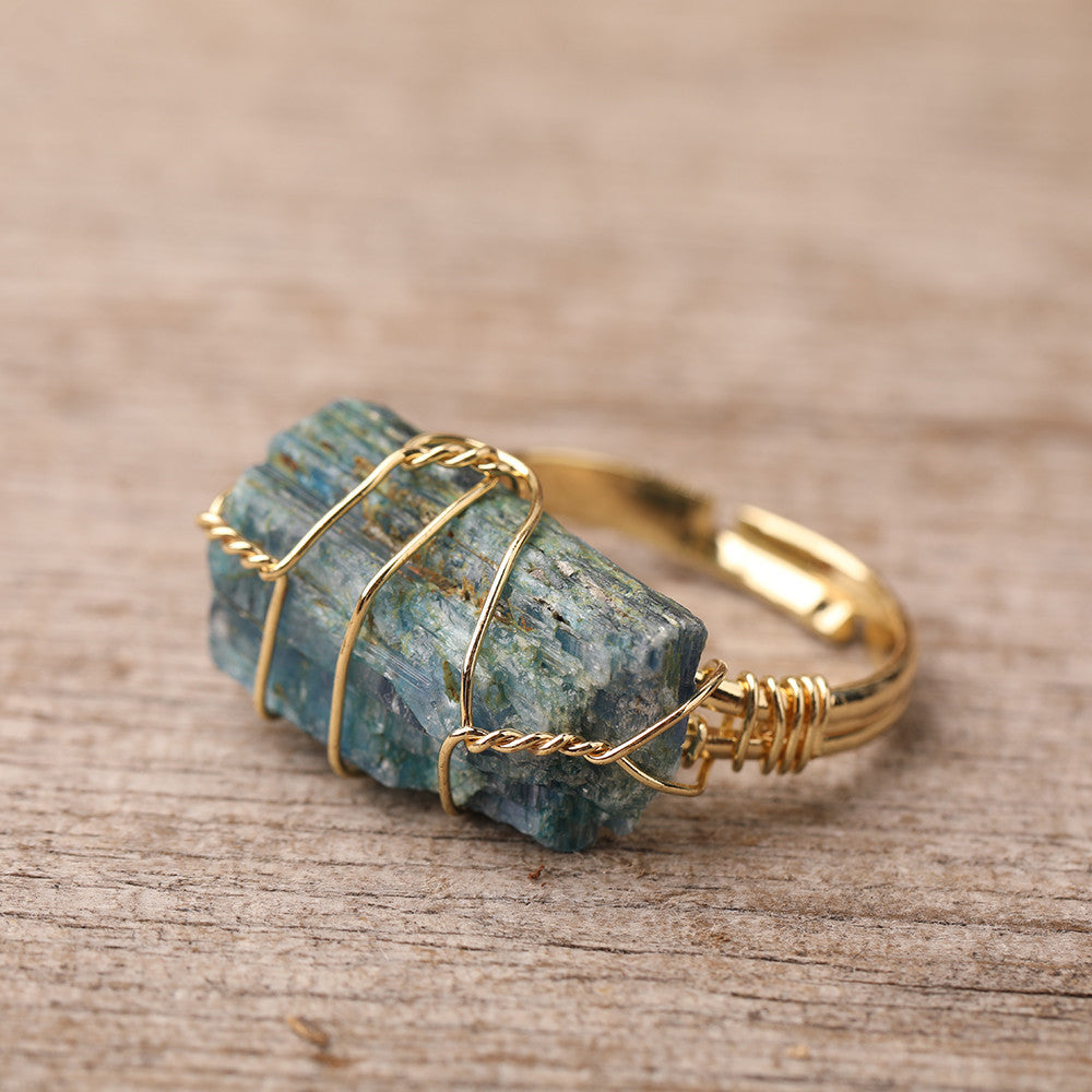 Natural Gemstone Gold Ring with raw blue kyanite stone wire-wrapped in gold, on wood surface