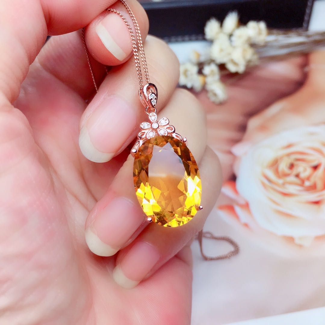 Close-up of citrine pendant with floral bail from the Crystal Pendant Necklace Set, held between fingers