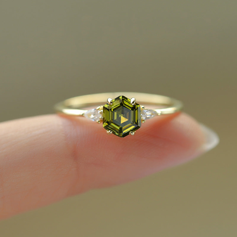 Close-up of hexagon-cut green gemstone ring with pear-shaped diamond accents on fingertip