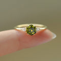 Close-up of hexagon-cut green gemstone ring with pear-shaped diamond accents on fingertip
