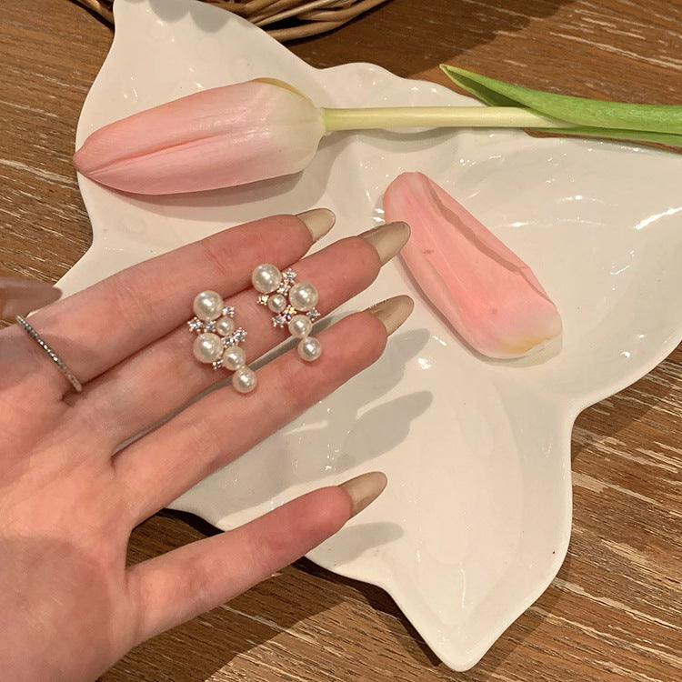 Pearl cluster earrings resting in open hand with pink tulip petal, styled flat-lay on wooden table