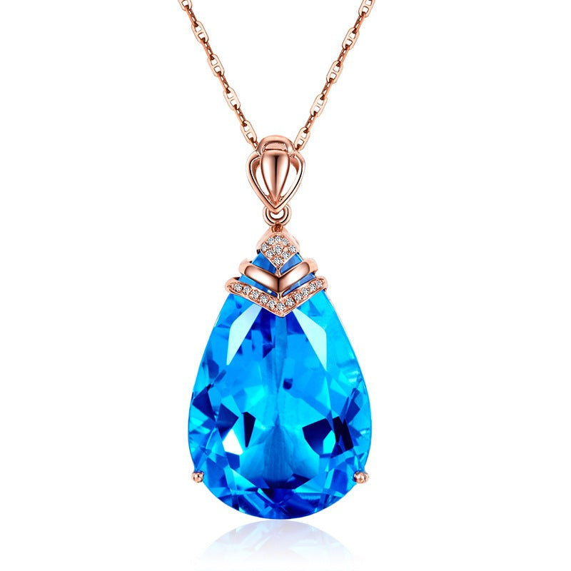 Blue Crystal Pendant Necklace on white background, pear-cut blue topaz with diamond-accent cap on rose-gold chain