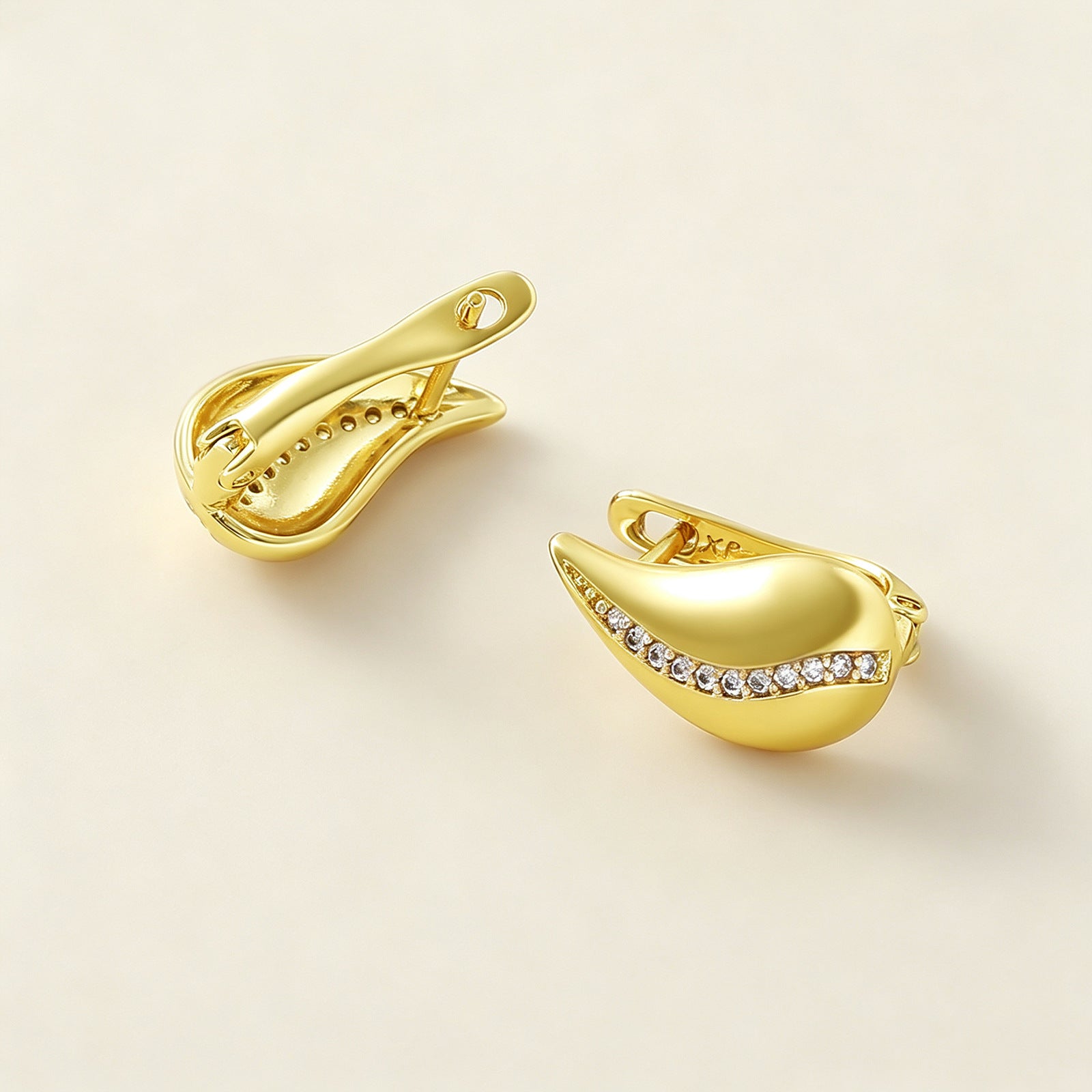 French Drop Earrings scattered on beige surface, angled view of gold swirl design with crystal accent