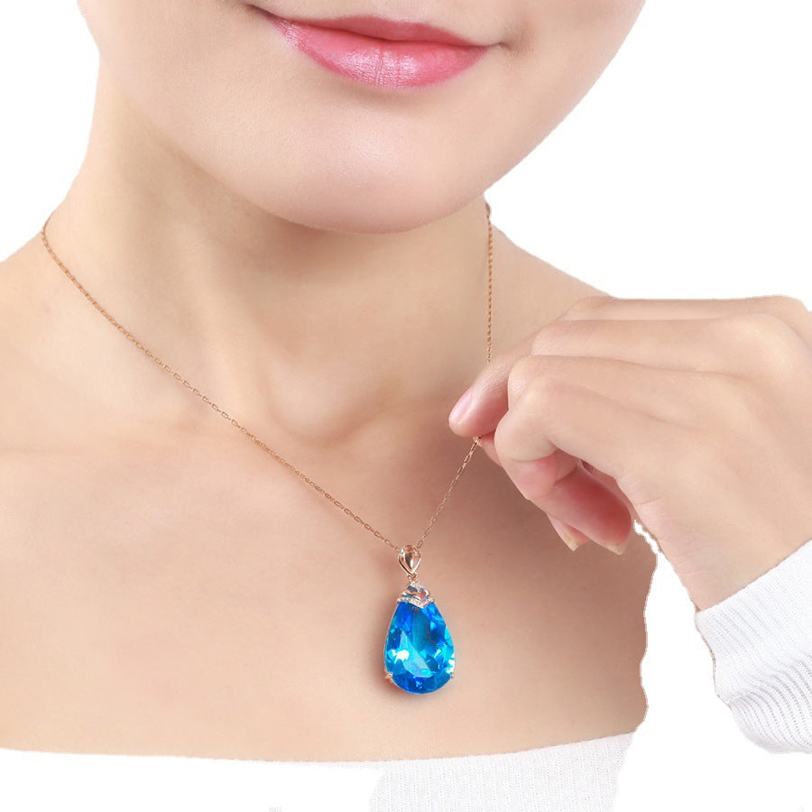 Woman wearing Blue Crystal Pendant Necklace, blue topaz teardrop pendant on rose-gold chain at collarbone