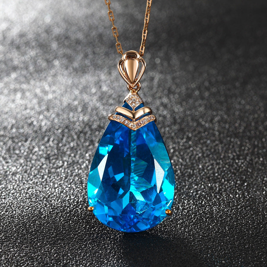 Blue Crystal Pendant Necklace close-up, pear-cut blue topaz pendant on textured gray stone surface