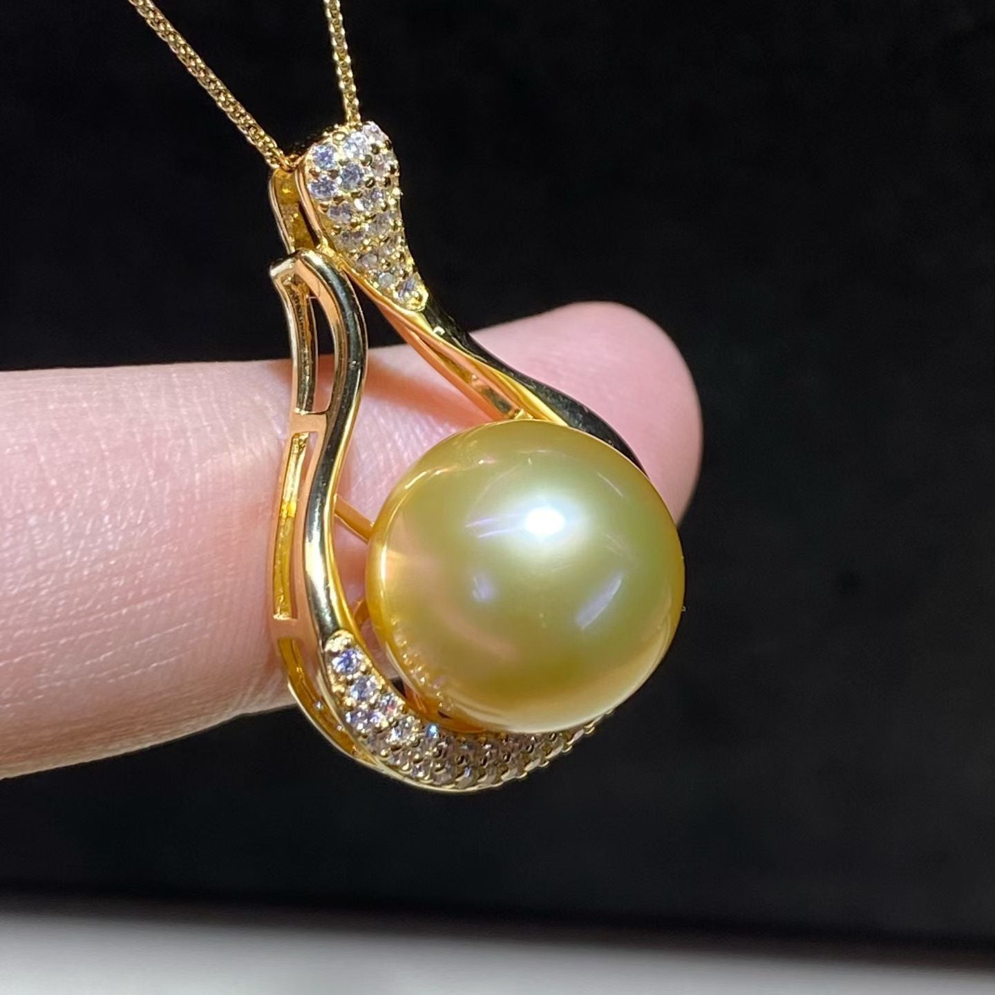 South Sea Pearl Necklace pendant in swirl-shaped gold and diamond setting, held on fingertip
